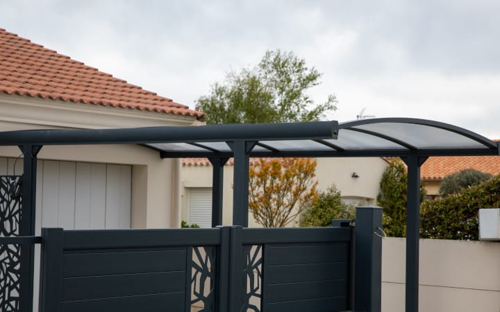 Auvent en aluminium et polycarbonate au dessus d'un carport à l'entrée d'une maison